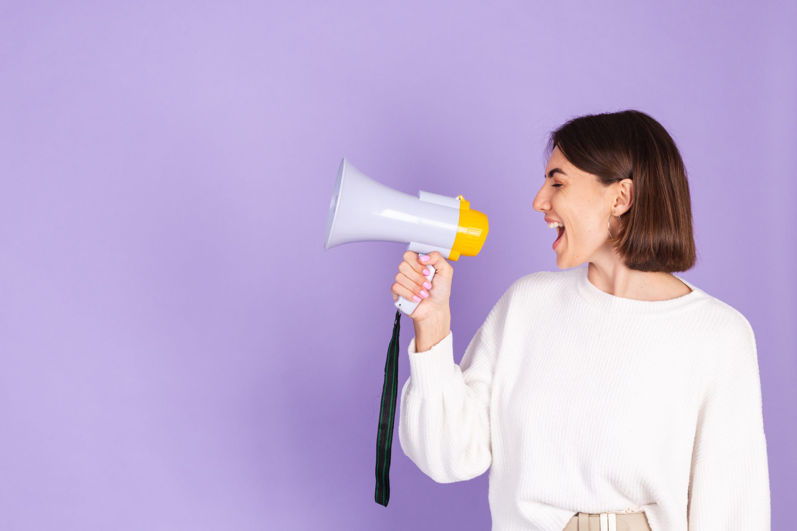 A young woman with a megaphone in front of a purple wall.